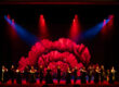Elenco de 25 artistas de la Compañía Flamenca Antonio Andrade bailando en el escenario de la Royal Opera House de Muscat durante el espectáculo Noches Flamencas, bajo iluminación escénica roja y azul con una gran flor proyectada de fondo.